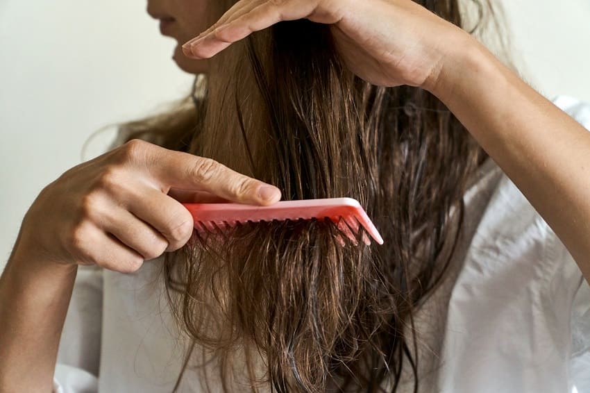 Eine Frau kämmt mit einem pinken Kamm ihr brüchiges Haar
